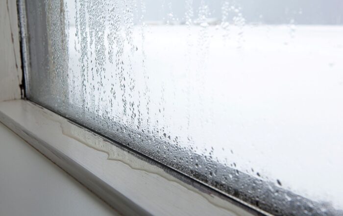 Condensation and moisture buildup along the bottom edge of a residential window, with water droplets on the glass and dampness visible on the window frame.